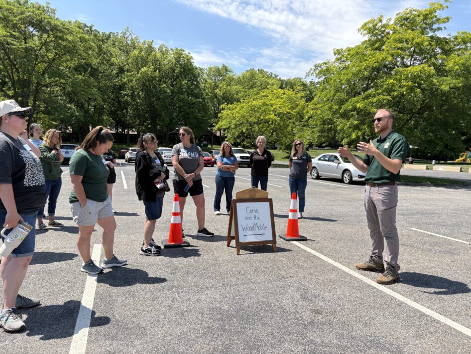 Educators stand in a parking lot outdoors near a sign that says "Come see the Wood Mobile."
