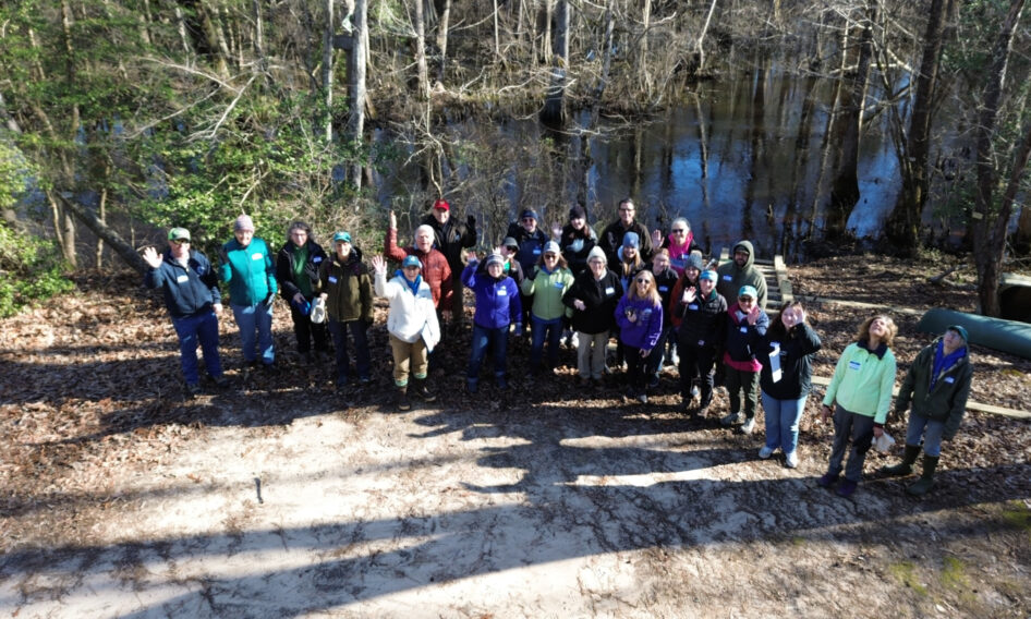 A group of community members look up at the camera within the forest along Dragon Run waterway.
