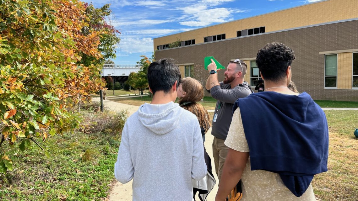 Sean Tracy leads a small group of teenagers on a walk near trees outside of a school building.