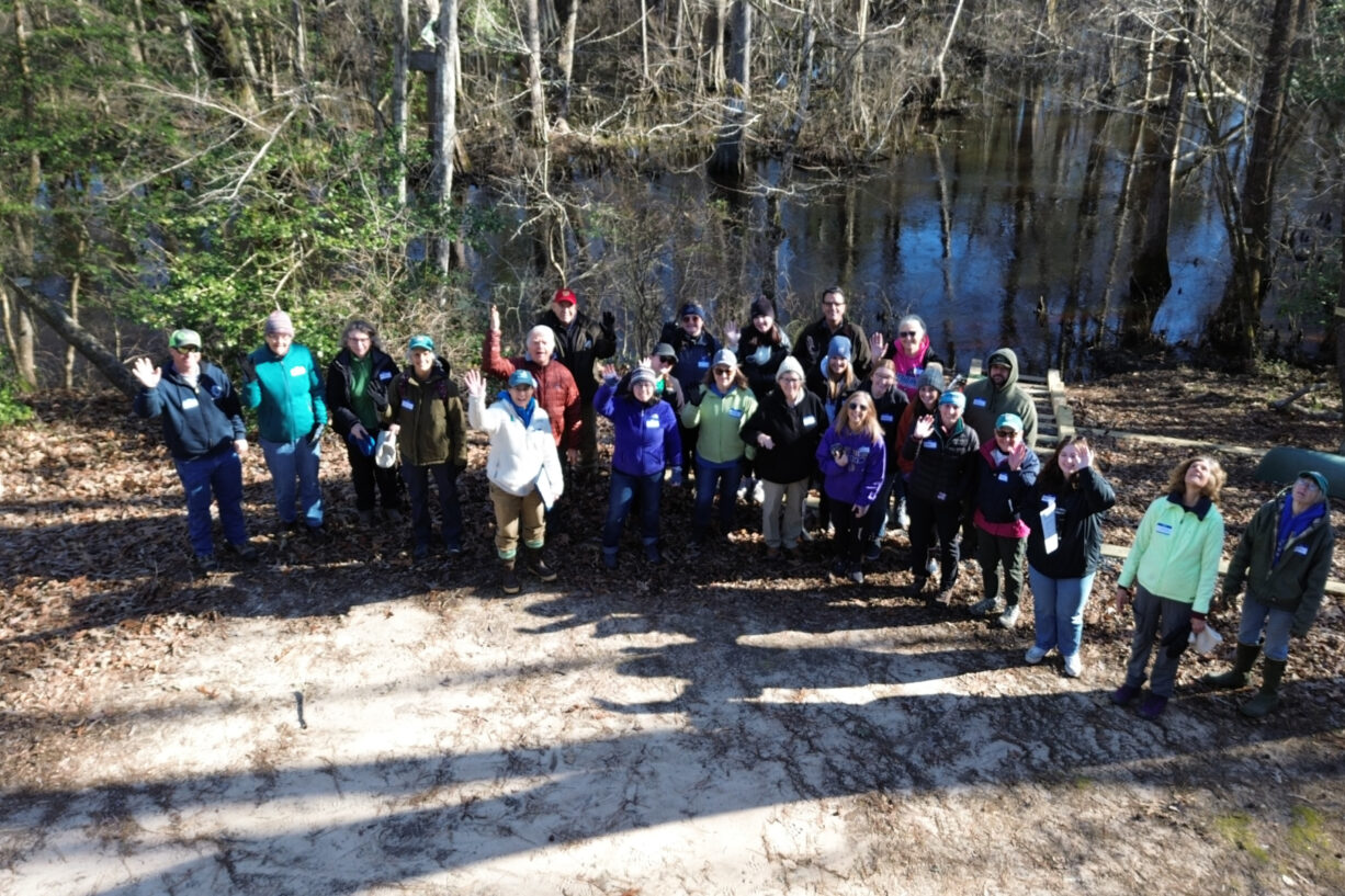 A group of community members look up at the camera within the forest along Dragon Run waterway.